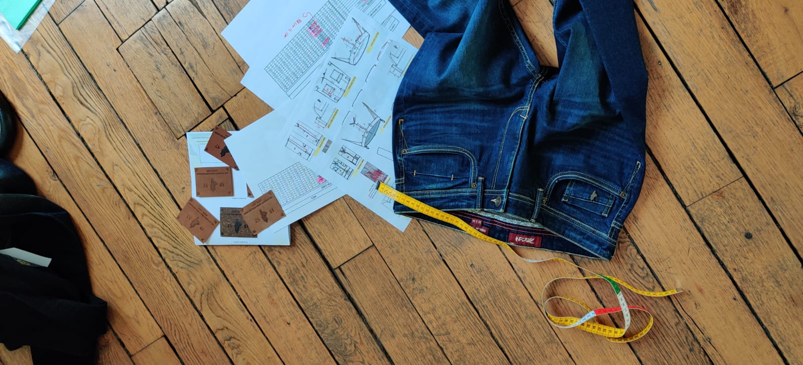 Étiquettes de marque en cuir, dossier technique et jean de référence posés à l'atelier